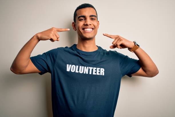 istockphoto-1214212565-612×612 Young handsome african american man volunteering wearing t-shirt with volunteer message smiling cheerful showing and pointing with fingers teeth and mouth. Dental health concept.