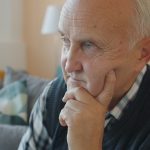 Elderly man with hand on chin, deep in thought.